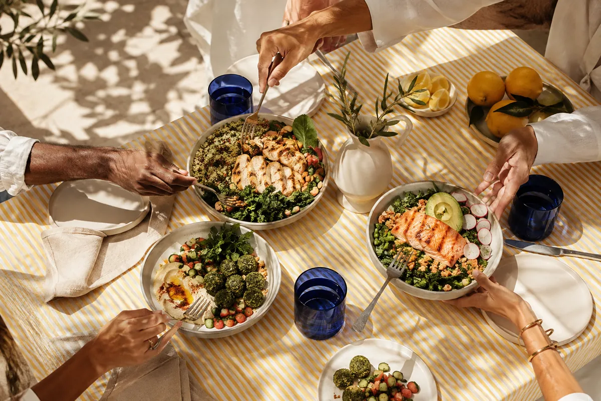 Hands sharing colourful food around a sunlit table
